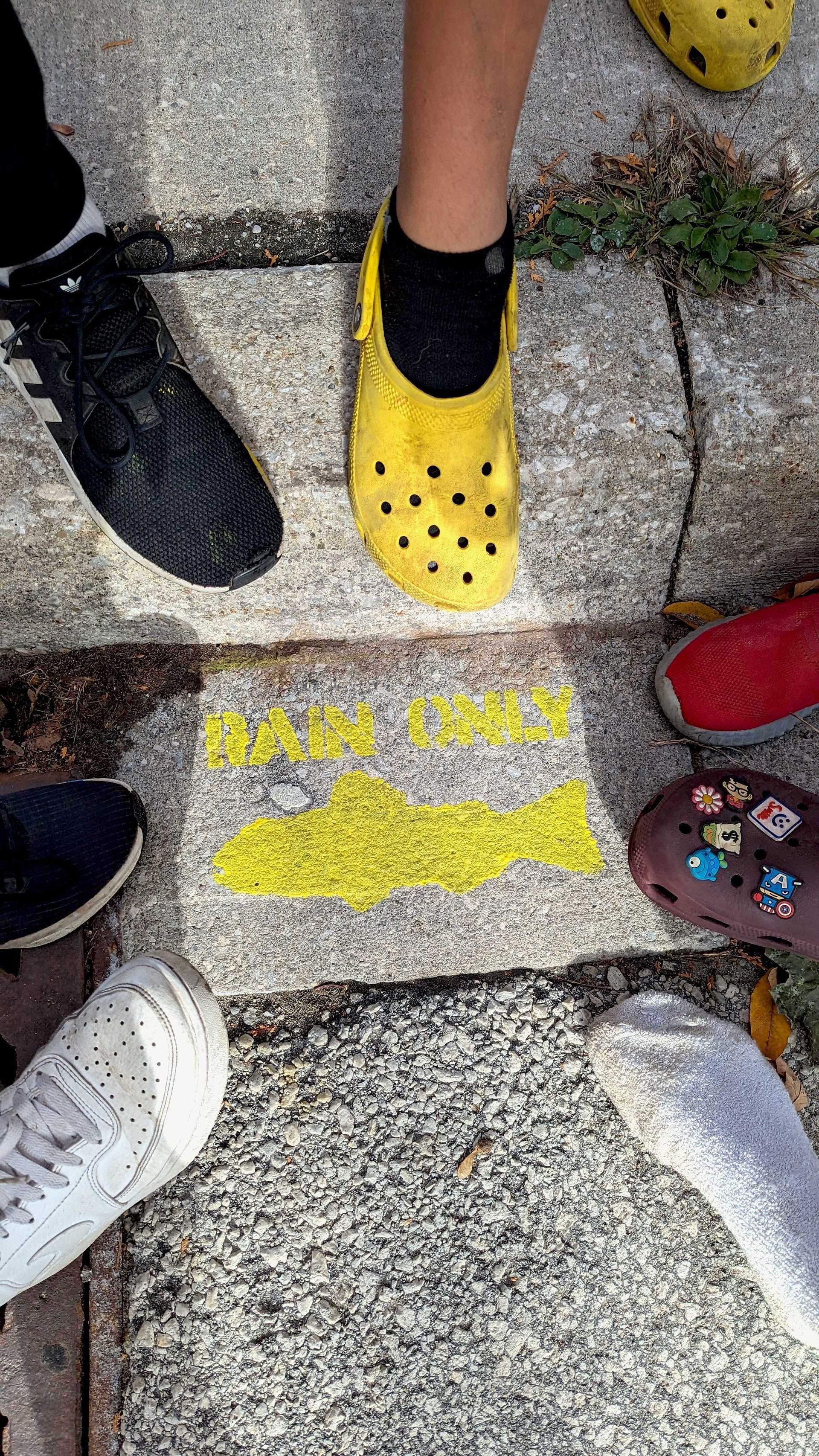 Feet in a circle around a painted yellow fish on the street