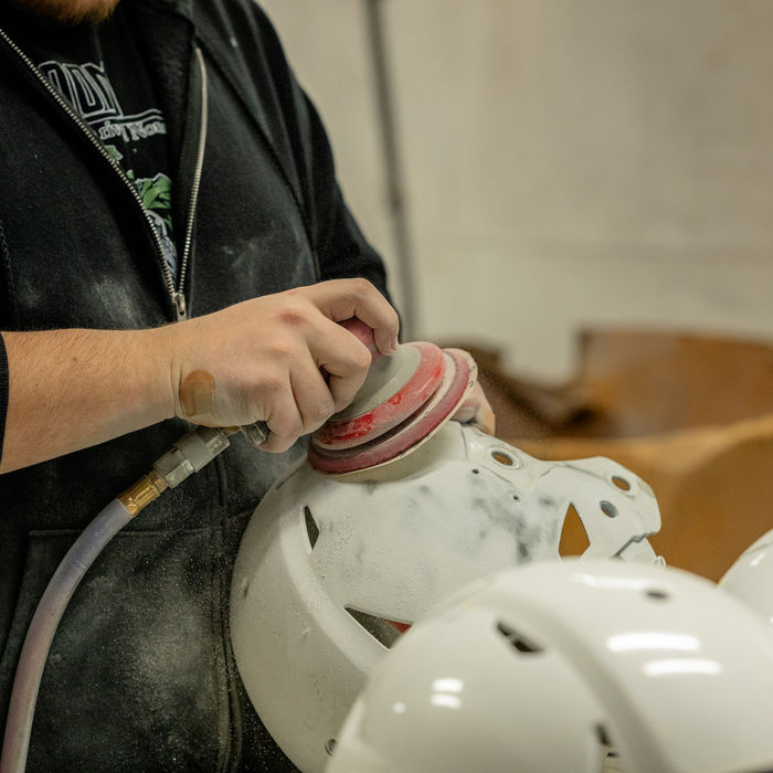Person sanding a white helmet with an orbital sander in a workshop.