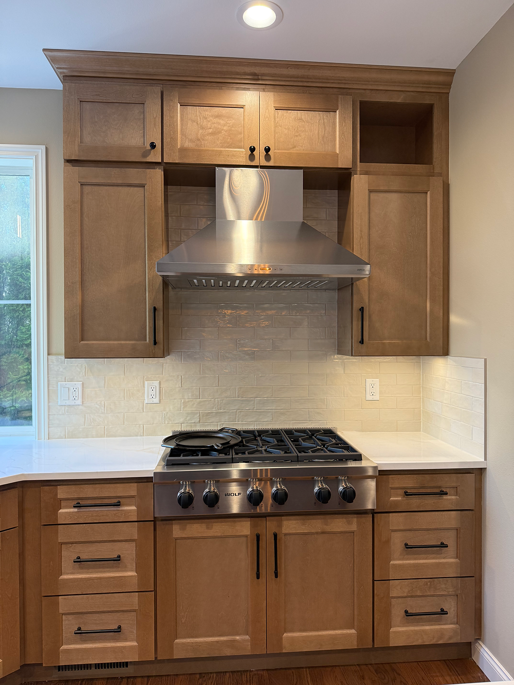 Gas range with wood cabinets, tile backsplash, and stainless steel hood in Sammamish kitchen remodel.