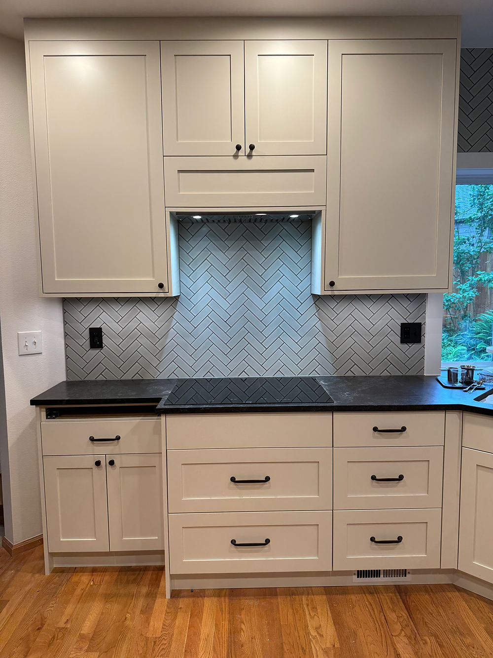 Gray kitchen cabinets with built-in range hood and quartz countertop in remodeled kitchen.