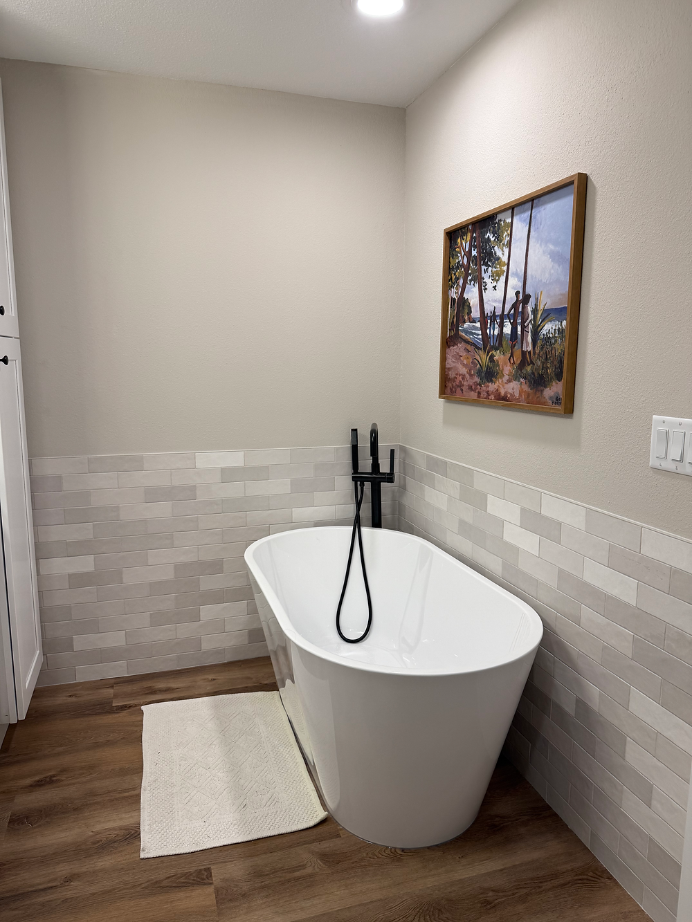 Freestanding white soaking tub in a modern bathroom with neutral walls and wood flooring.