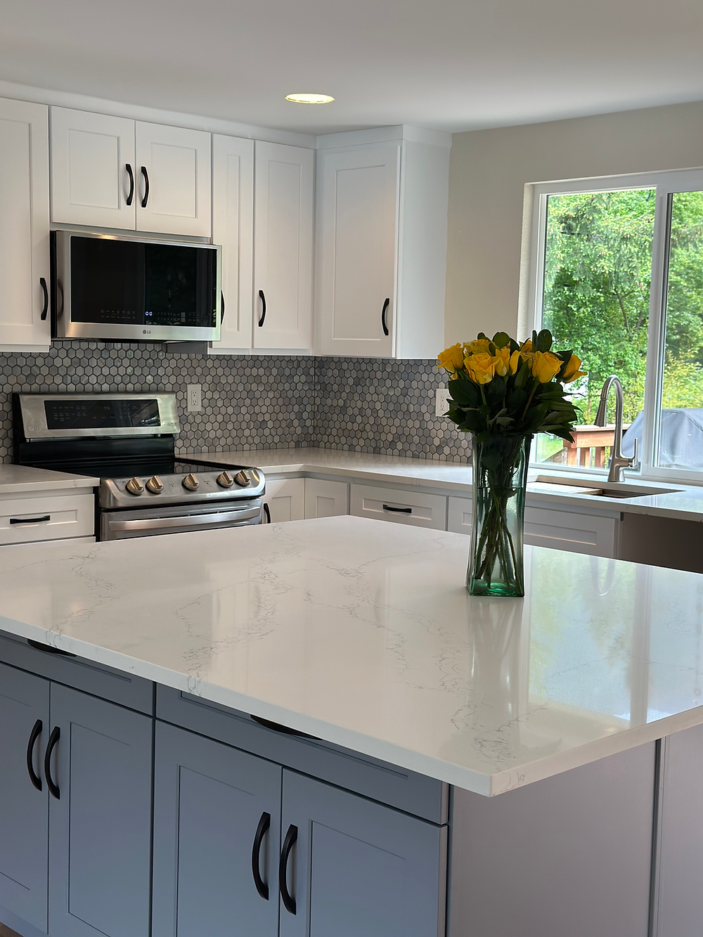 Kitchen island with quartz countertop, shaker cabinets, and modern lighting in a bright remodeled kitchen.