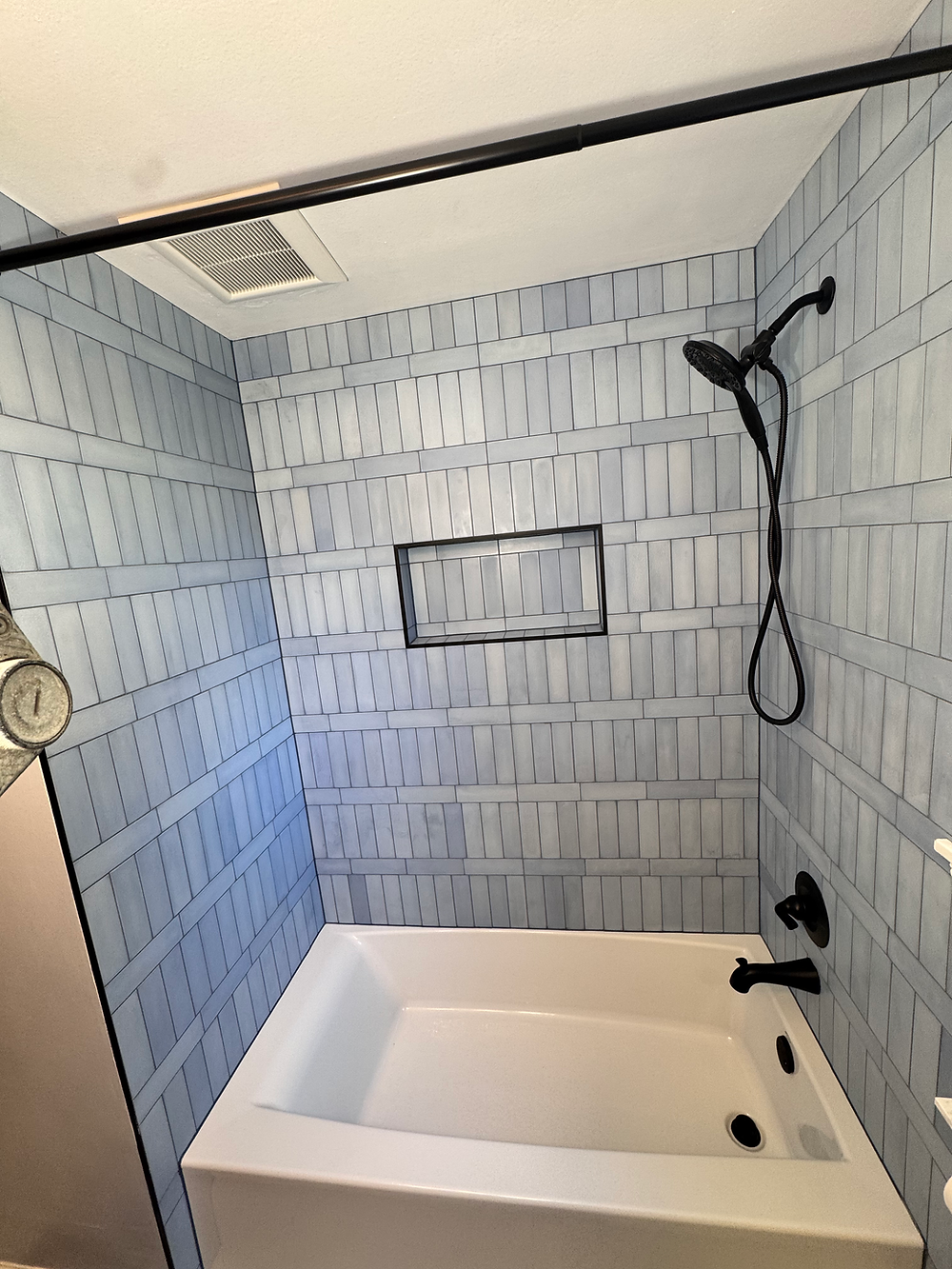 Bathtub with gray tiled walls, recessed niche shelf, and matte black fixtures.