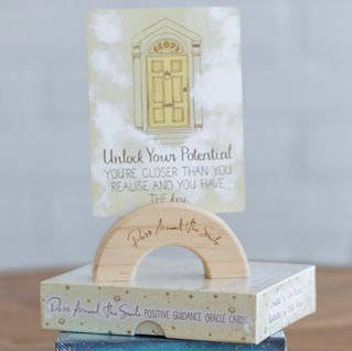 A small wooden arch shaped oracle card holder with cards against a plain background.