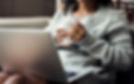 person sitting with an open laptop on their lap. They are holding a mug of tea.