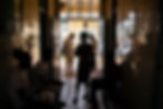 Patients waiting outside a pharmacy are seen in silhouette as sunlight streams through the doorway.