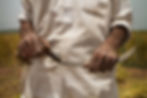 A farmer holds a sickle in a field. The frame focuses on his weathered hands and tools.