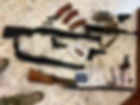 Several firearms, ammunition magazines, documents and a device with wires are laid out on a tiled floor.