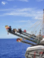 Workers hang perilously from poles of a vessel as part of squid fishing operation.
