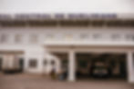 An ambulance is parked at the entrance of a hospital, while a few people stand outside the building, partially visible.