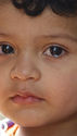 A child looks directly into the camera with tears in eyes.