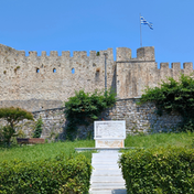 Exterior view of Arta Castle with massive fortress walls, battlements, a Greek flag and a landscaped park in the foreground.