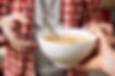 Hands holding a bowl of soup with a spoon in it.