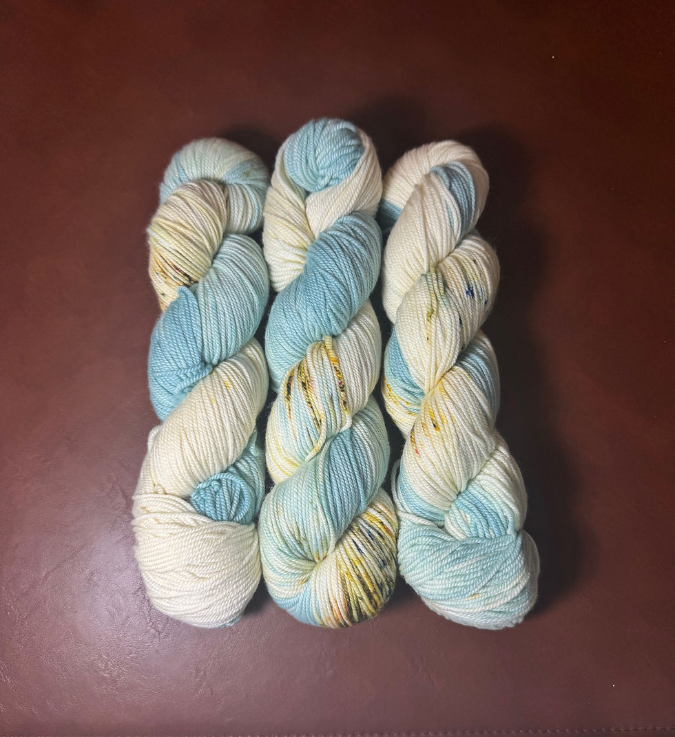 Three skeins of hand dyed yarn in soft blue, cream, and speckled yellow-green, inspired by water, sand, and life in a desert.