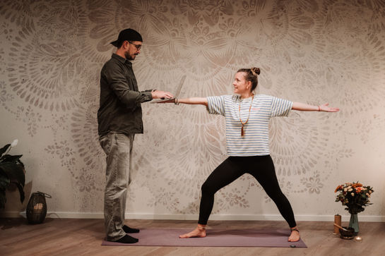 Warrior‑II‑Pose mit humorvollem Moment im Yogastudio.