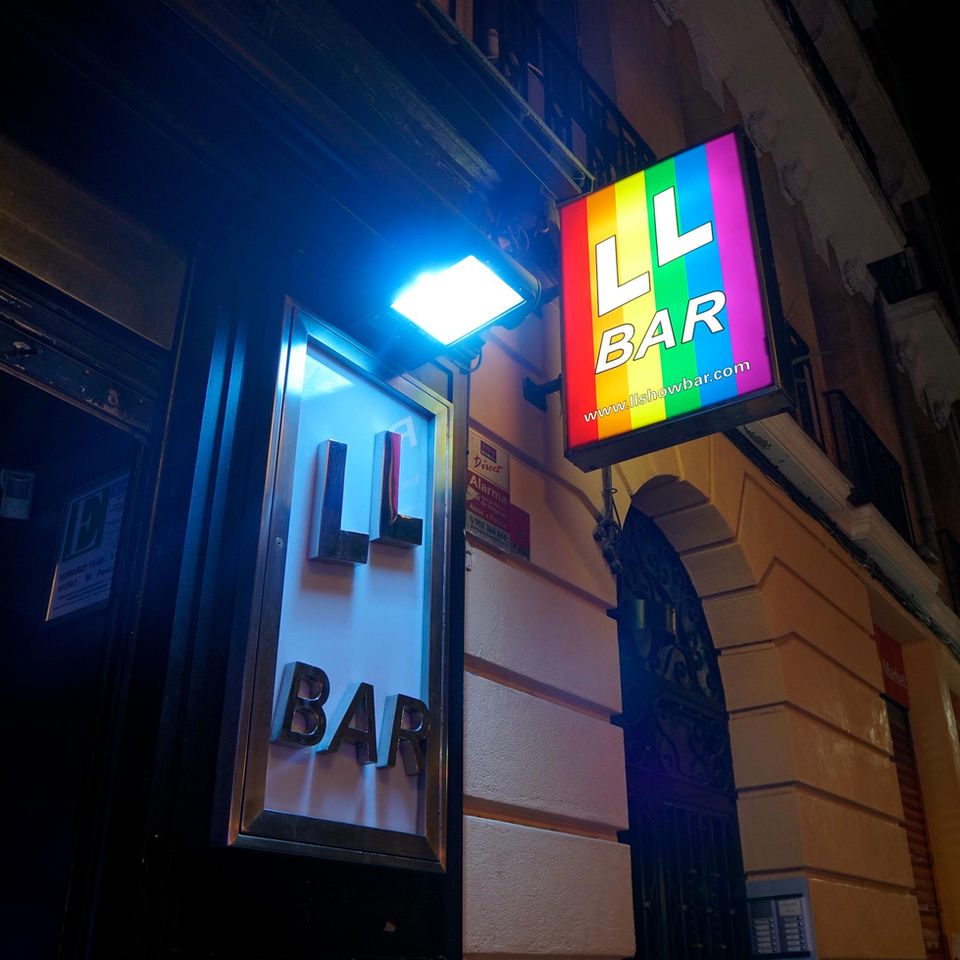 Fachada del LL Bar durante la noche y el mítico cartel del local con la bandera LGTBIQ+ iluminada en la calle Pelayo de Madrid