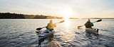 Two people kayaking on open water toward a golden sunset