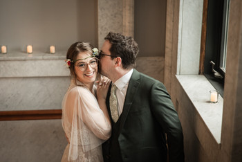 Groom kissing bride on cheek in front of window and marble wall