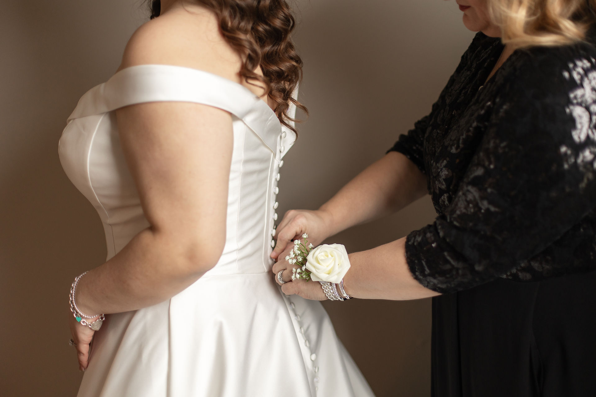 Close up of buttons on elegant wedding dress with the brides mother helping to button the buttons. 
