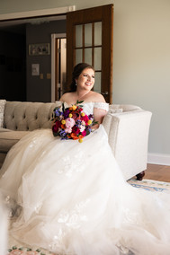 Bride with red, pink and white boquet sitting on couch with train falling on the ground 