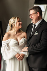 Father of bride holding his daughters arm and looking at each other while laughing