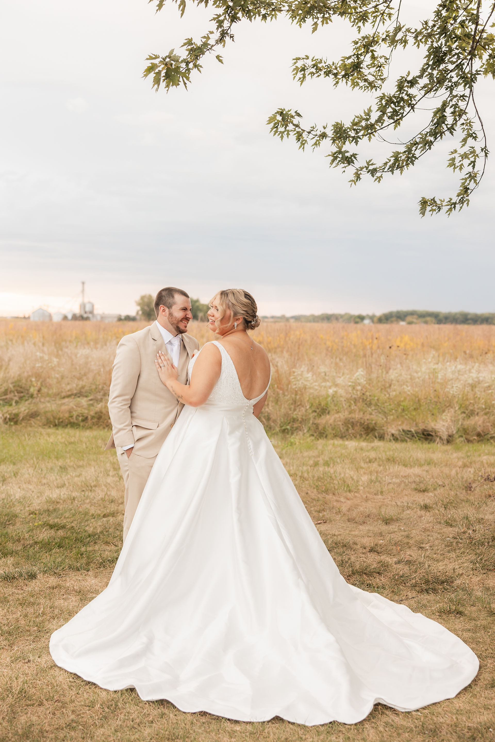 Bride with large train spread out facing groom in front of a field