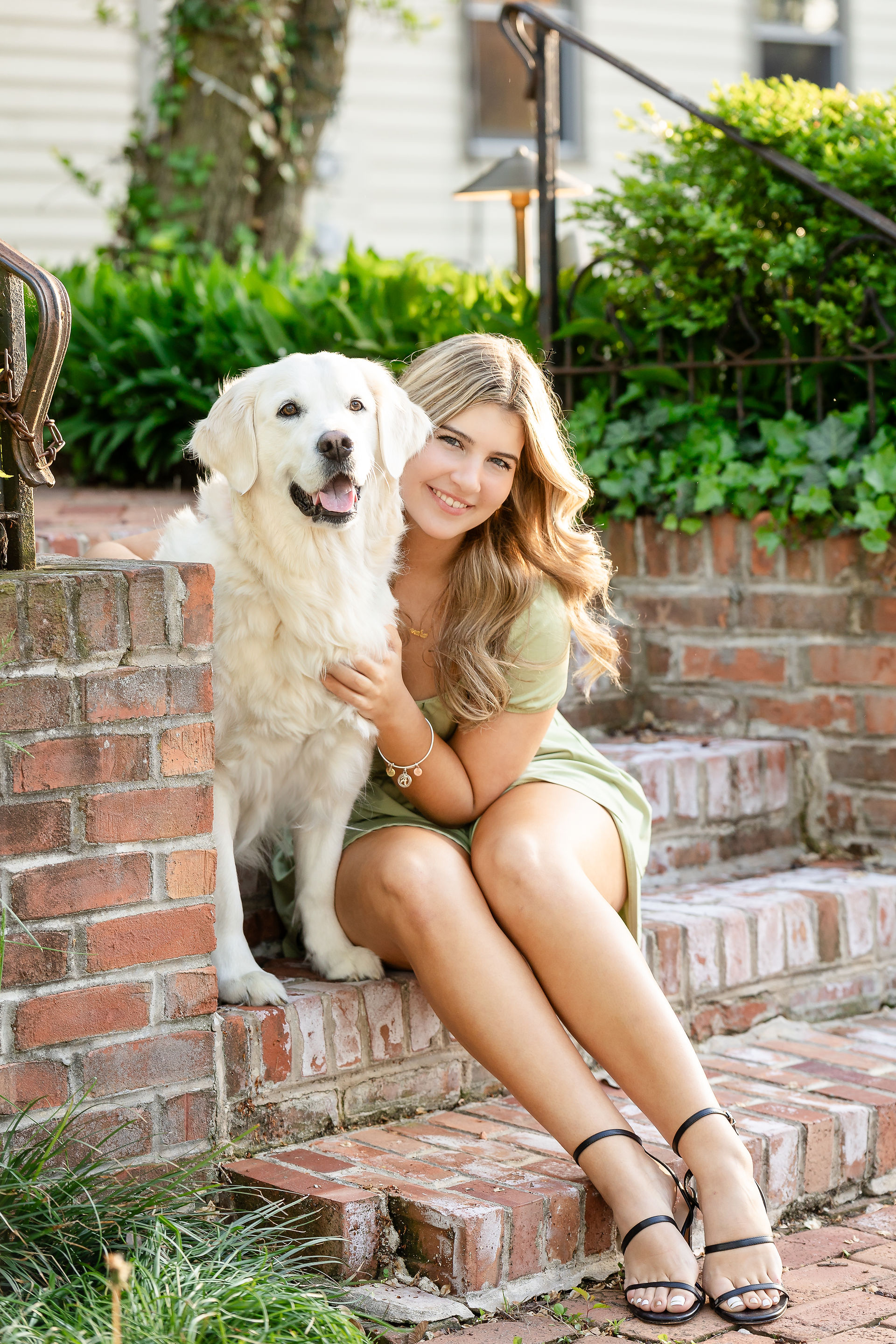 Senior photo of female subject and her white fluffy dog sitting on brick stairs
