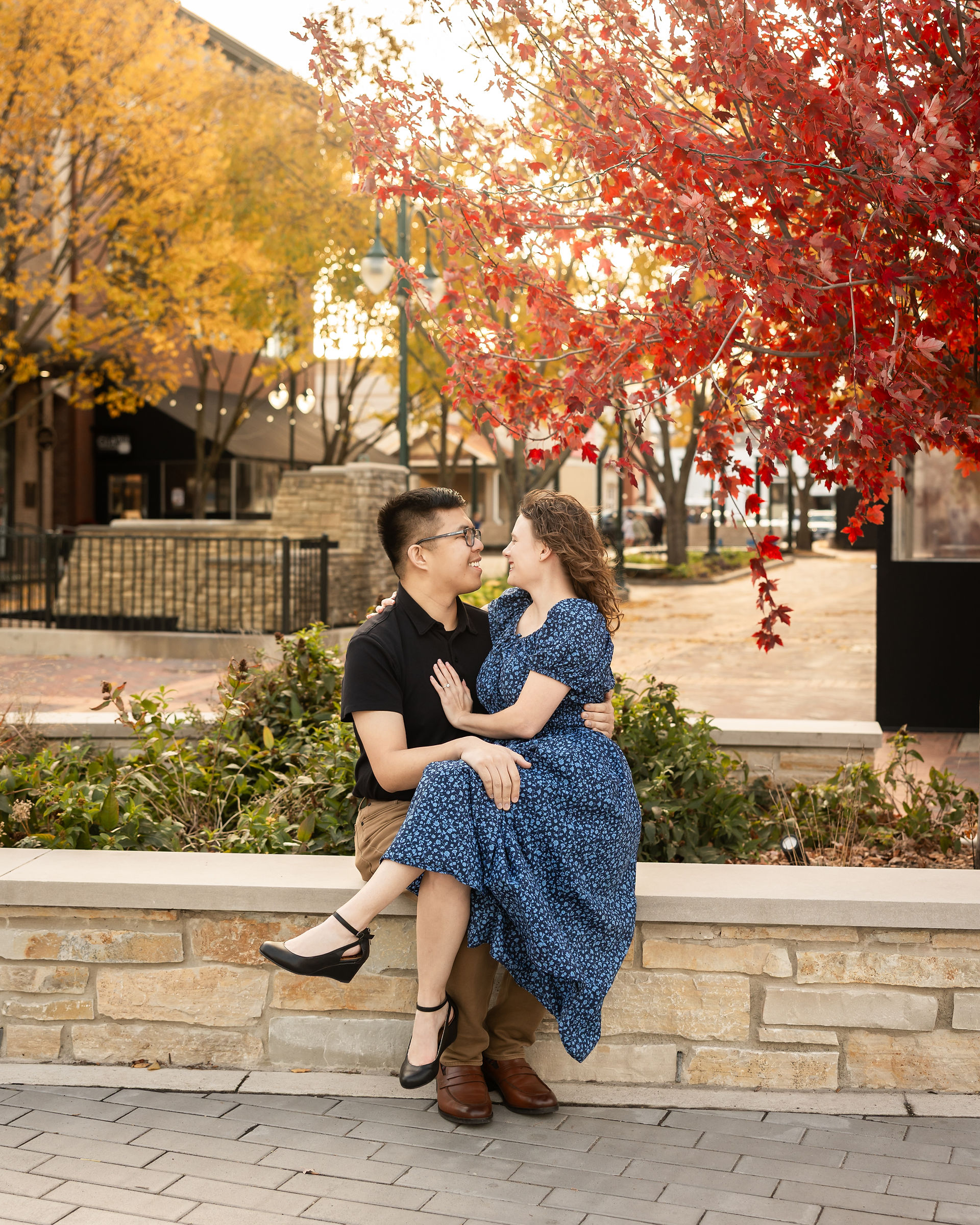 Romantic couple pose of couple sitting together on a ledge with fall foliage in the background