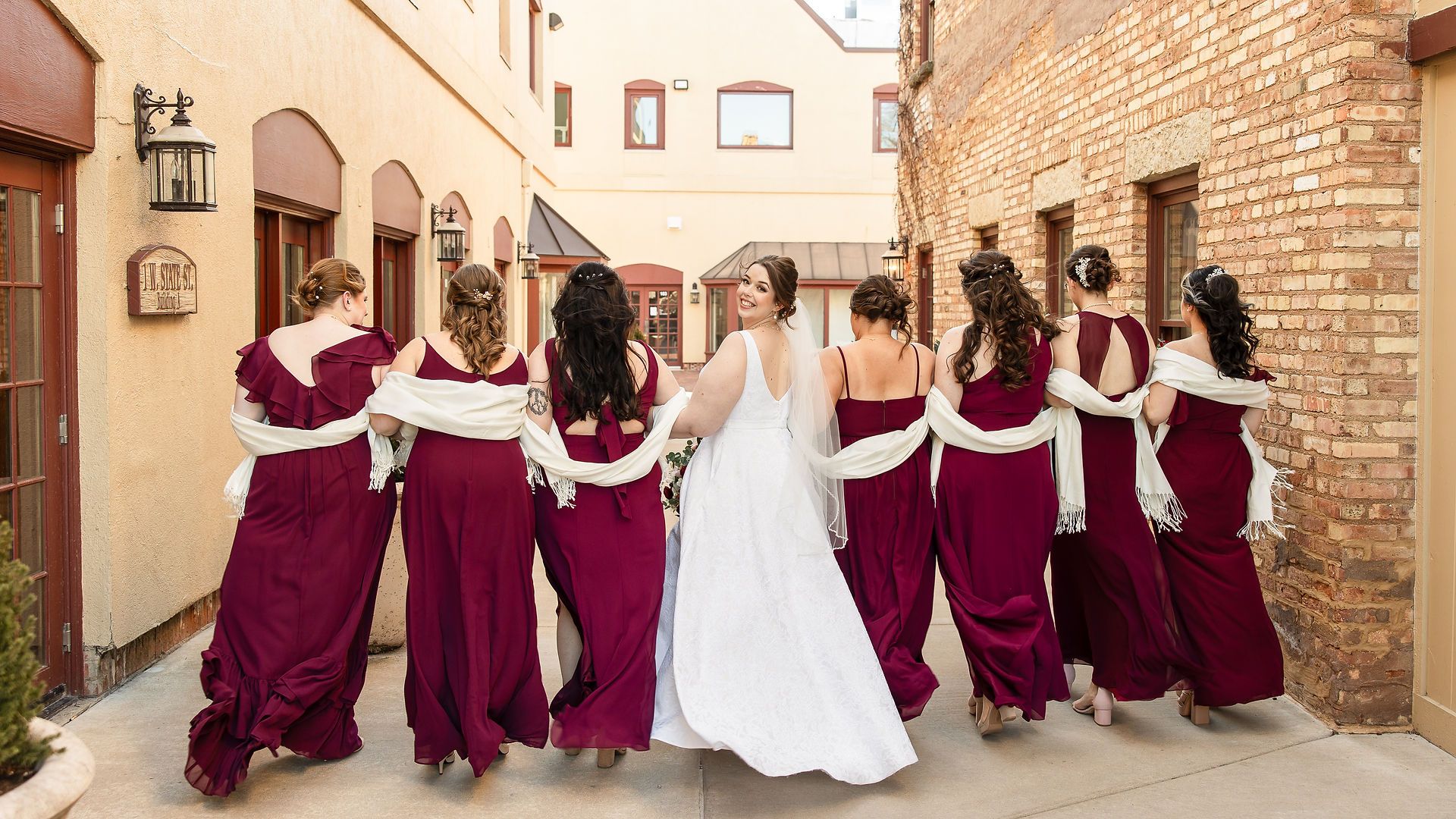 bride and bridesmaids walking away while linking arms with bride looking back