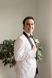 groom with a white tuxedo standing by a window