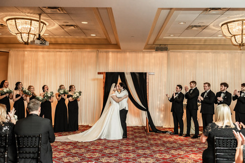 bride and grooms first kiss as husband and wife. Wide photo with wedding party and guests clapping