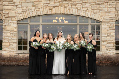 bridesmaids wearing black dresses standing with bride in front of stone wall 