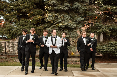 groom in white tux with groomsmen in black tuxes walking towards the camera 
