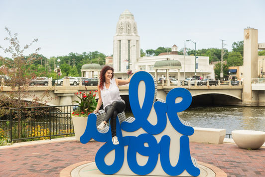 Branding photo of a hair stylist in downtown St. Charles IL on top of the "Be You" Sign with the municipal building in the background