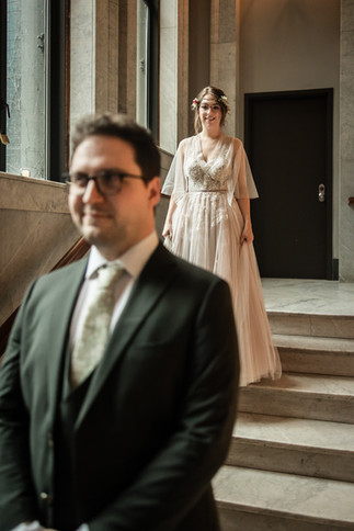 Bride standing behind groom before first look on marble stairs at Newberry library in Chicago