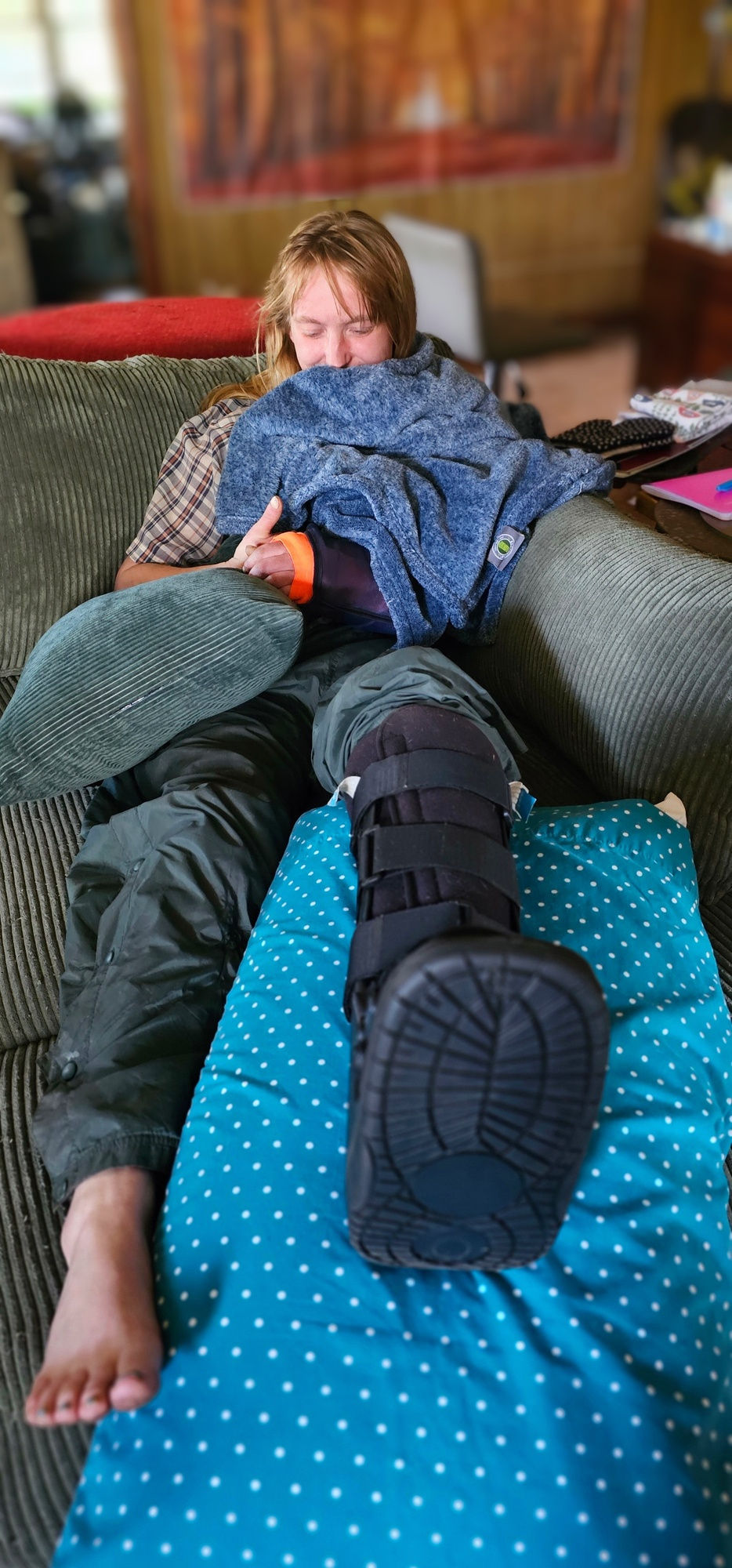 Dana giving a thumbs up, with a blanket over her cast to warm it, on her new comfy chaise.