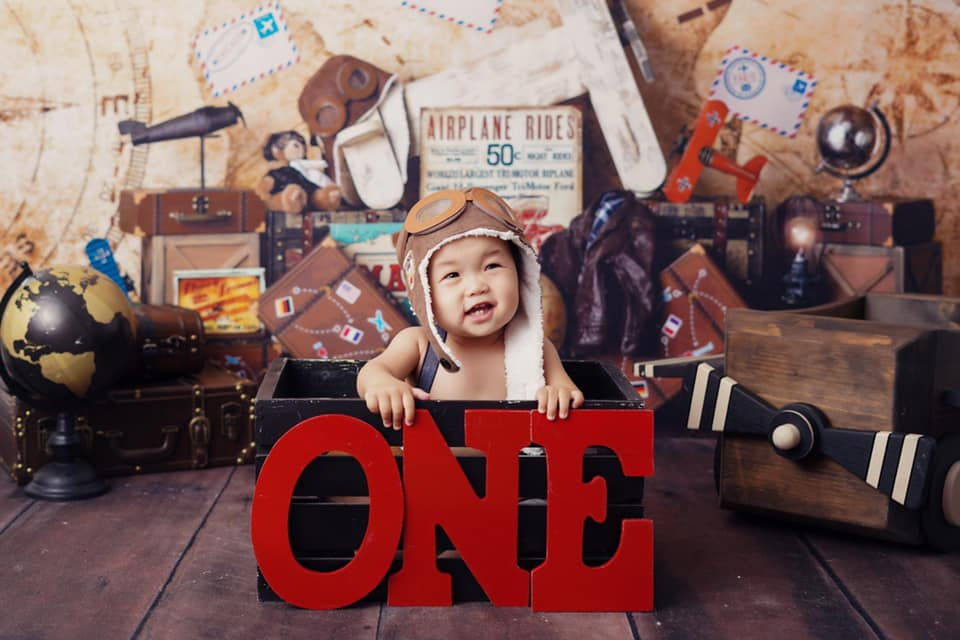 Baby in a leather aviator cap peeking from a wooden ONE crate on a vintage airplane-rides set during a Folsom first birthday cake smash session