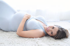 Expectant mother in a soft blue draped top reclining on a plush rug during studio maternity photos