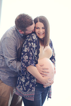 Expectant couple sharing a kiss as the father cradles the baby bump and mother wears a floral kimono during studio maternity photography