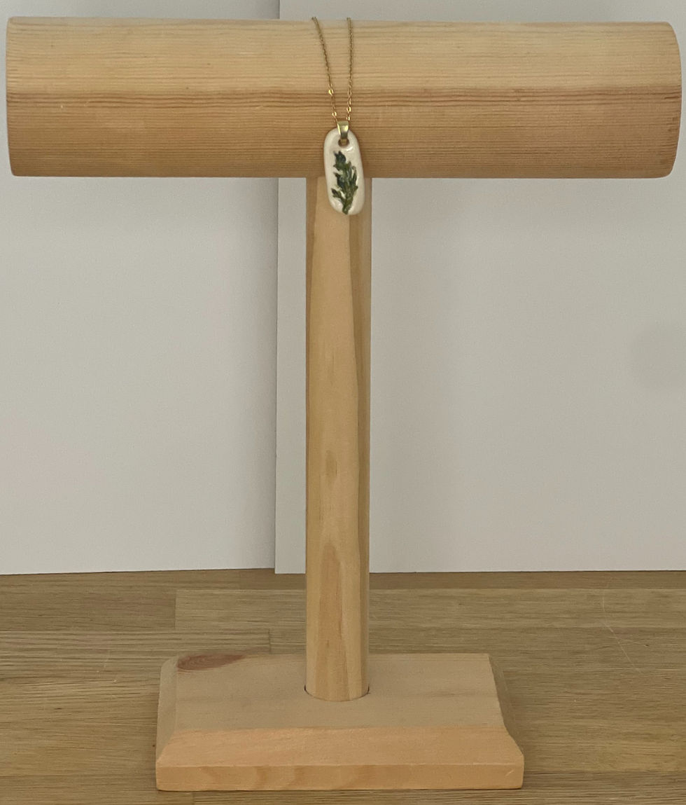 Un collier sur un présentoir en bois, avec une feuille. Dans ma bulle de terre