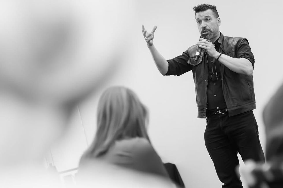 S. Scott Mason speaks into a handheld microphone and reaches toward the audience during a leadership presentation.