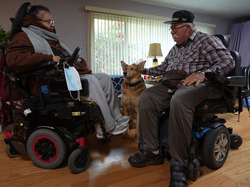Two people in wheelchairs, one petting a dog