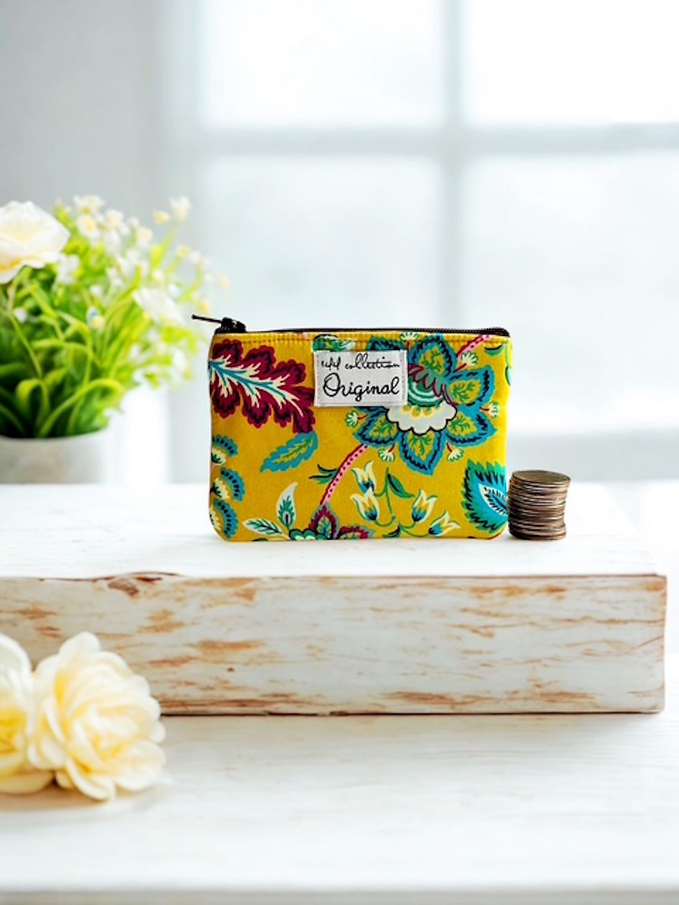 yellow jacobean floral cloth coin purse on a white wooden table next to coins and flowers