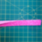 A long piece of pink binding fabric, folded over, but slightly open on one end to show the wrong side of the fabric inside.