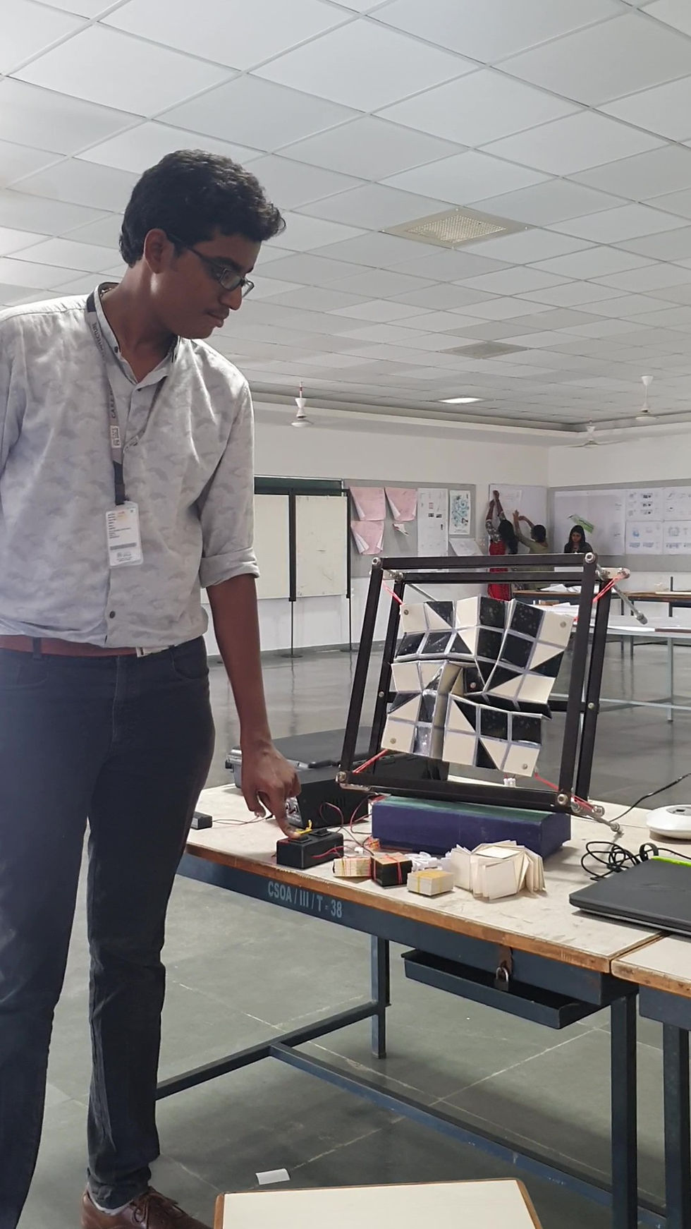 A working mechanical prototype of a black-and-white origami flasher dynamic facade module mounted inside a structural test rig with motor controls.