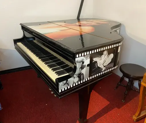 Black and white Knabe grand piano with striking Marilyn Monroe and vintage Hollywood artwork on the cabinet.