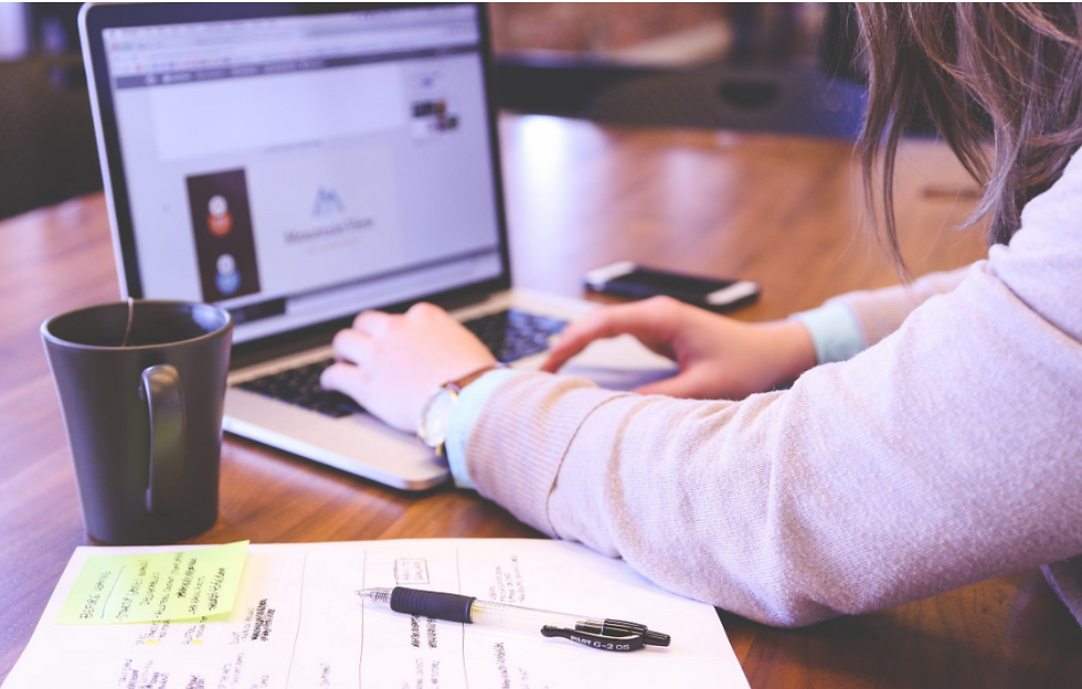 Person typing on a laptop beside a mug and handwritten notes