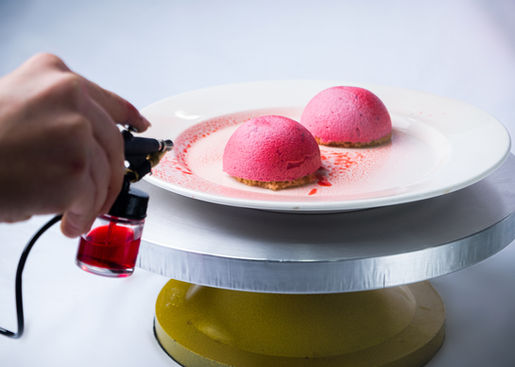 Chef rociando postre con aerosol rojo, sobre plato blanco, PORTAFOLIO FOTO. Primer plano.foto gastronómica 