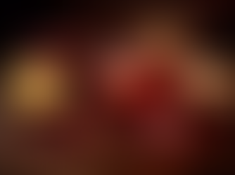 1954-inspired, deep-red hibiscus bourbon cocktail served in a rocks glass over ice, surrounded by lemon, pomegranate seeds, ginger root, and hibiscus petals on a moody wooden bar.