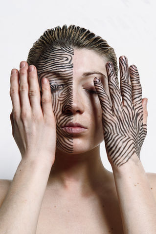 Photograph of a girl with half her face painted by The Line Girl in black Lines and her left hand also painted in black lines